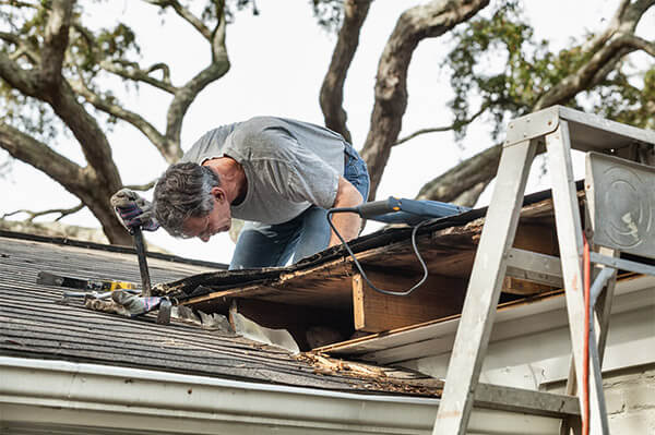 A man up on a damaged roof with some tools